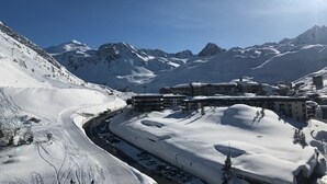 A snow-covered mountain resort with a ski lift, buildings, and a clear blue sky.