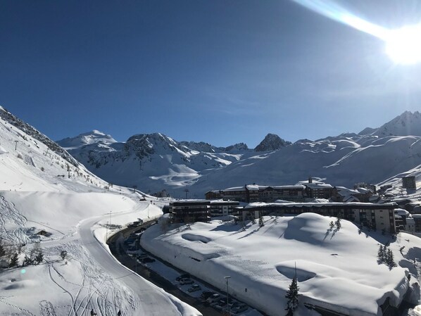 A snow-covered mountain resort with a ski lift, buildings, and a clear blue sky.