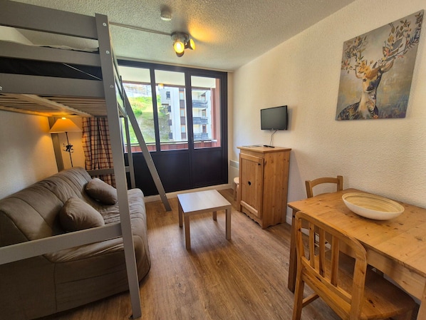 A cozy room with a bunk bed, a wooden table, a chair, a television, and a painting on the wall.