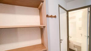 Ein Zimmer mit einer Holzboden, einer weißen Wand, einer Einbaureihe und einer Tür zu einem Badezimmer mit einer Badewanne.