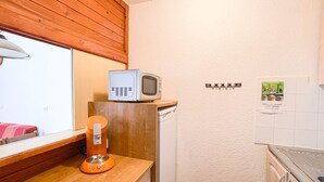Eine kleine Küche mit Mikrowelle auf einer Holzausziehtafel, einem kleinen Kühlschrank und einem Fenster mit Jalousien.