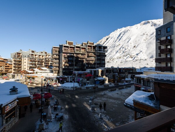 A snowy mountain town with multi-story buildings, a central square with outdoor seating, and a mountain backdrop.