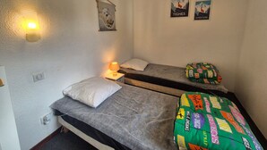 A small, compact room with two single beds, a wall-mounted light, and two posters on the wall.