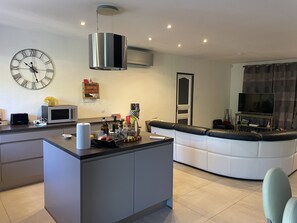 Una cocina moderna con una isla central, un área de comedor con un sofá y una sala de estar con televisor.