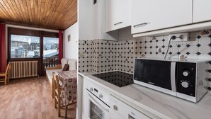 A compact kitchen with white cabinets, a microwave, and a Bosch oven. There's a dining area with a table and chairs, and a view of a snowy landscape through a window.