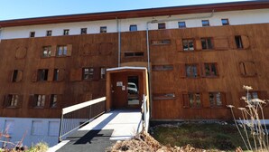 A multi-story building with a wooden facade, a central entrance with a ramp, and a clear sky.
