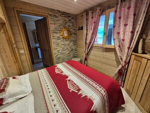 A bedroom with a bed, a stone wall, a wooden door, and a window with curtains.