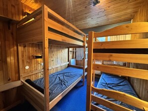 A room with bunk beds, wooden walls, and a blue carpet.