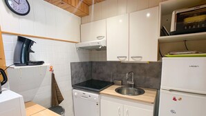 Cocina compacta con armarios blancos, estufa negra, un lavamanos y lavavajillas.