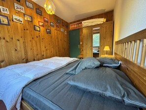 A wooden-paneled room with a bed, a wall-mounted lamp, and a door leading to another room.