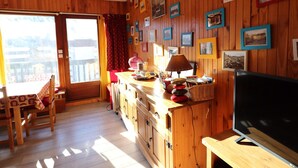 Un interior de madera con televisor, armarios de madera y una zona de comedor con mesa y sillas.