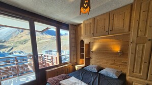 Un dormitorio con un ventanal grande, paredes de madera, una cama con almohadas y una mesita de noche.
