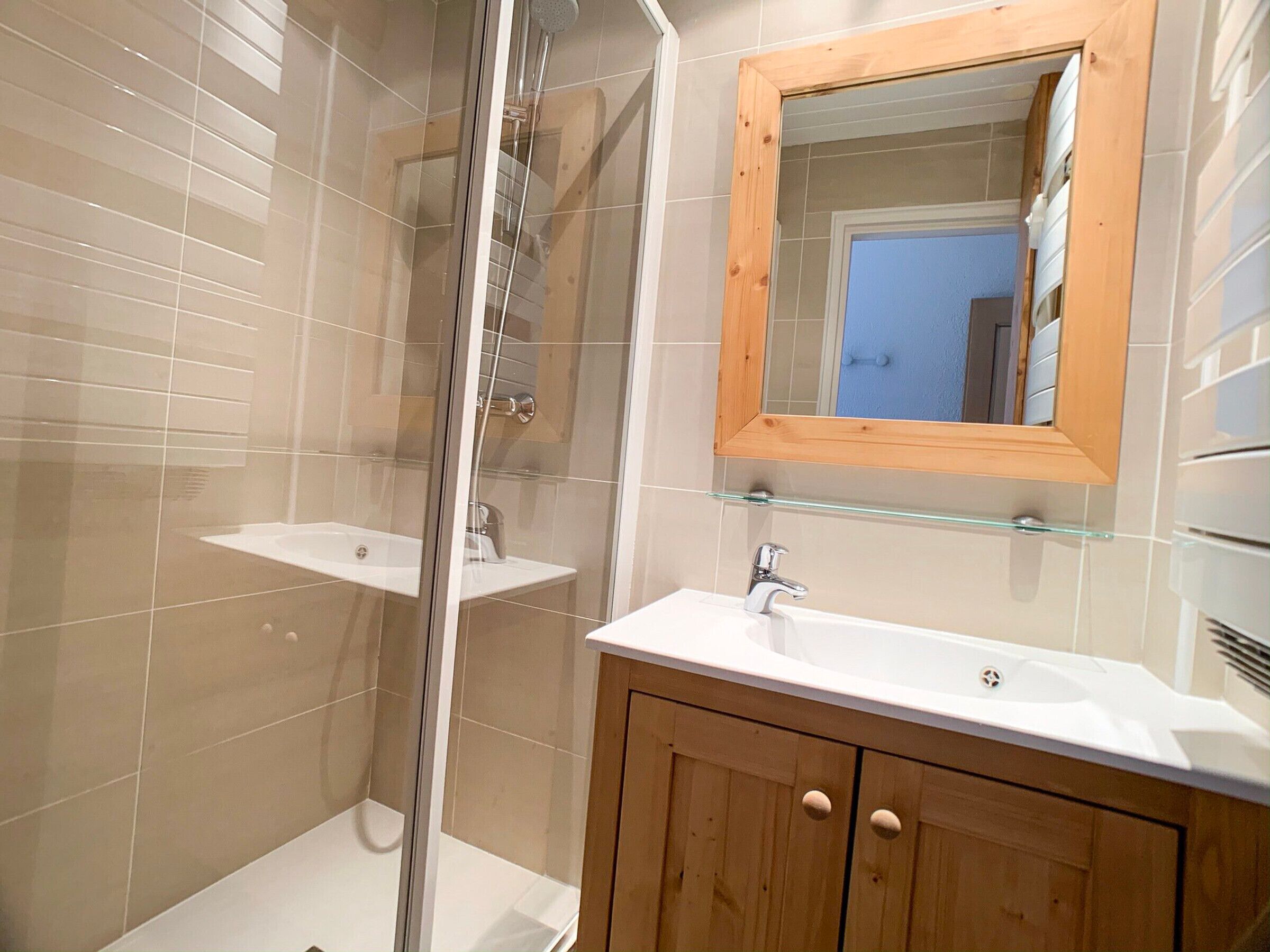 Un baño con cabina de ducha de vidrio, tocador de madera con espejo y lavabo blanco.