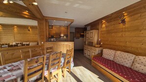 Acogedor interior de cabaña con mesa de comedor de madera, sillas, sofá y zona de cocina.