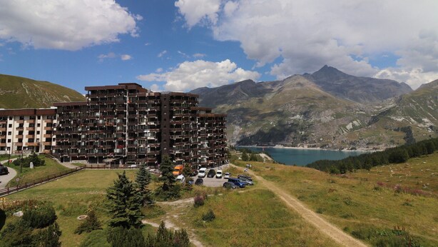 A multi-story hotel with balconies, a parking area, and a view of mountains and a lake. - Renovated Studio 2 Pers. Close to Slopes with Balcony (Tignes)