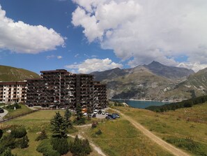 A multi-story hotel with balconies, a parking area, and a view of mountains and a lake.