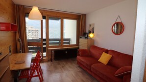 A cozy living area with a wooden table, red chairs, a red sofa, and a large window offering a city view. - Renovated Studio 2 Pers. Close to Slopes with Balcony (Tignes)