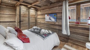 Quarto estilo cabana de madeira com cama, almofadas, um quadro e vista para o exterior.