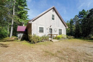 Une maison en bois d’un seul étage, avec un toit à pignon, un porche à l’avant et une petite terrasse.