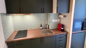 Une cuisine de taille réduite, avec des meubles de couleur sombre, un plan de travail en bois, un évier et un four à micro-ondes.