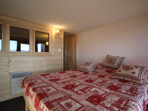 Quarto com parede de madeira, uma janela, cama com roupa de cama estampada e luminária fixada na parede.