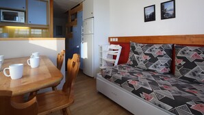 A compact room with a wooden dining table, chairs, a sofa with patterned cushions, a microwave, and a refrigerator. - Quiet Duplex with Balcony - 6 pers, Charmettoger (Les Arcs 1800)