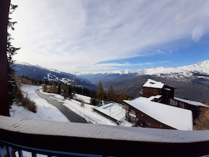 Vista de montanhas com estrada, edifícios e picos cobertos de neve.