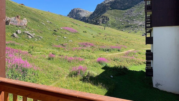 Un paysage de montagne avec un sentier, un bâtiment doté d’un balcon et un ciel dégagé.