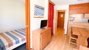 Une petite pièce comprenant un lit, une armoire en bois, un téléviseur et un coin cuisine.