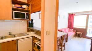 Une cuisine compacte équipée d’un four à micro-ondes, d’une machine à café et d’un petit réfrigérateur. On y trouve une table à manger en bois avec des chaises, ainsi qu’une petite fenêtre donnant sur un paysage agréable.