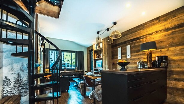 Une cuisine moderne avec un intérieur en bois, un îlot central noir et un escalier en colimaçon.