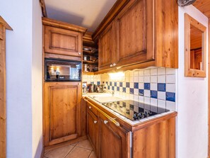 Una cucina compatta con mobili in legno, forno integrato e pannelli posteriori in piastrelle.