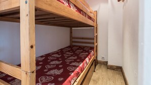 A bunk bed with a red patterned bedspread in a room with white walls and a wooden ceiling.