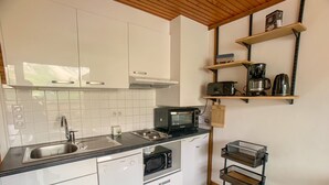 A compact kitchen with white cabinets, a black countertop, a Bosch dishwasher, a microwave, a coffee maker, and a small shelf with kitchen items.