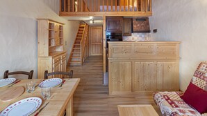 A cozy cabin interior with a dining area, wooden staircase, and a kitchen.