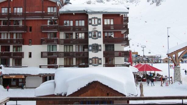 Un hôtel à plusieurs étages, doté de balcons, avec une piste de ski en arrière-plan.