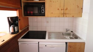 Une cuisine compacte dotée d’armoires en bois, d’un four à micro-ondes, d’une machine à café et d’un lave-vaisselle.