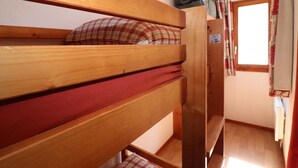 Un lit superposé avec un matelas rouge et un oreiller à carreaux, une tête de lit en bois et une fenêtre avec des rideaux.