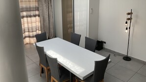 A modern dining area with a white table and grey chairs, a sliding glass door, and a standing floor lamp. - Villa Oceane 4 Chambres (San-Nicolao)