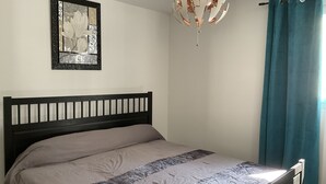 A bedroom with a bed, a hanging light fixture, a framed picture on the wall, and a window with curtains. - Villa Oceane 4 Chambres (San-Nicolao)