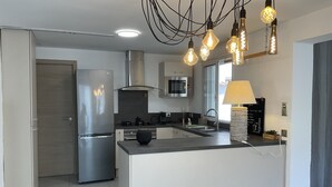 A modern kitchen with a central island, stainless steel appliances, and pendant lighting. - Villa Oceane 4 Chambres (San-Nicolao)