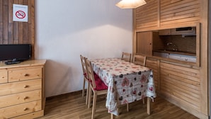 Eine kleine Küche mit Holzschränken, einem Esstisch mit gemustertem Tischläufer und einem Fernseher auf einer Holzkommode.