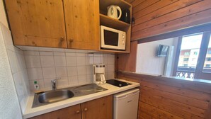 A compact kitchen with wooden cabinets, a microwave, a coffee maker, and a dishwasher.