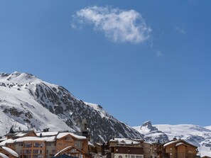 Montaña nevada con cielo azul despejado. Se observan edificios de madera con nieve en los tejados, probablemente un complejo de esquí.