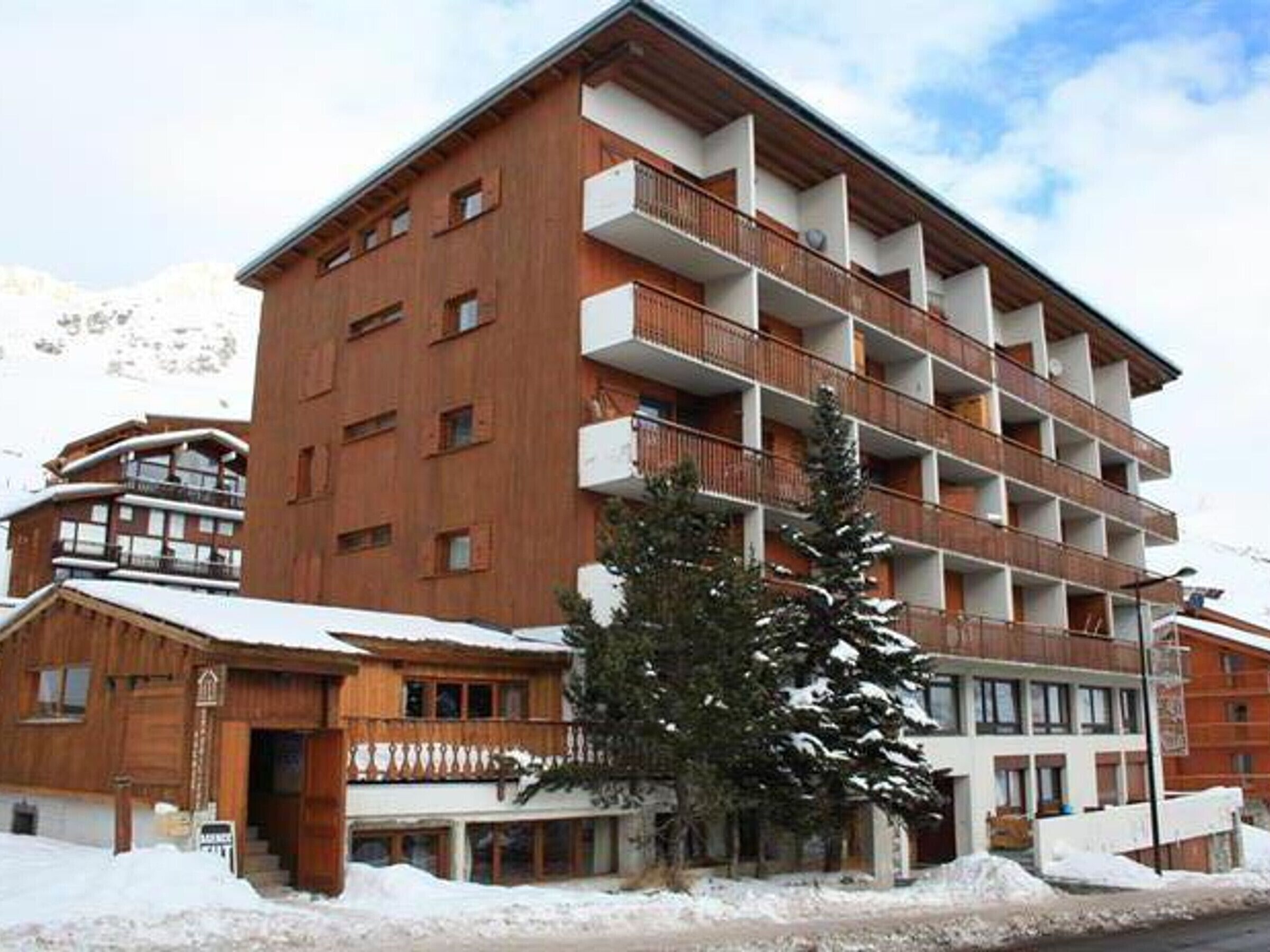 A multi-story hotel with balconies, a wooden facade, and a mountainous backdrop.