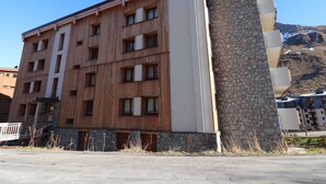 Hotel de vários andares com fachada de madeira e detalhes em pedra, com varandas e montanhas ao fundo.