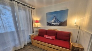 A cozy room with a wooden bed, a red pillow with "LOVE." on it, a painting of a mountain, and a lamp on a bedside table. - Renovated studio with balcony, near slopes, pets allowed (Tignes)
