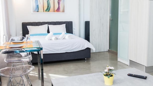 A modern hotel room with a bed, a dining table with chairs, a small table with a remote control, and a potted plant. - Beautiful Apt. close to Monastiraki (Athens)