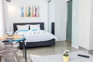A modern hotel room with a bed, a dining table with chairs, a small table with a remote control, and a potted plant. - Beautiful Apt. close to Monastiraki (Athens)