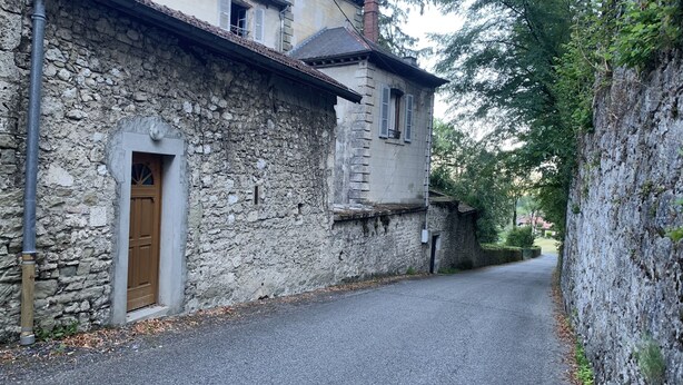 Eine enge Gasse mit Steinhäusern, einer Holztür und einer Metallrohrleitung.